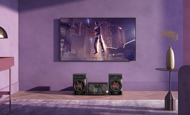 LG CK43N is placed on the living room. Above the speaker, LG TV is hung on the wall showing a movie scene.