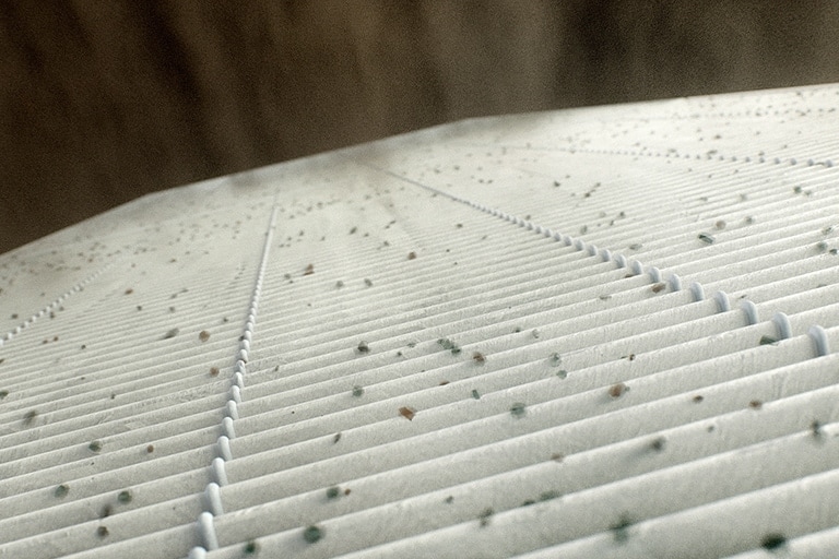 A multitude of 1-3 μm particles has adhered to the surface of the white MERV 13 filter.
