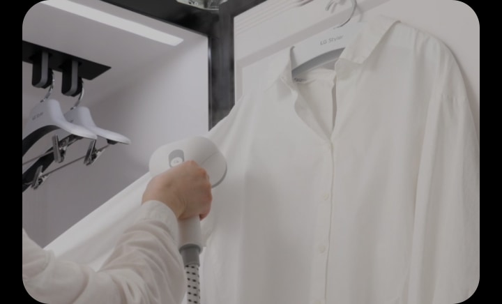A person using built-in handy steamer in LG Styler to remove wrinkles from shirt with adjustable pressure settings