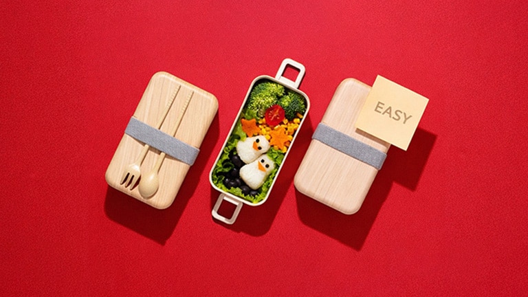 An image showing an easy bento box meal with penguin-shaped rice balls and colorful vegetables on a red background, illustrating a simple meal-prep concept.