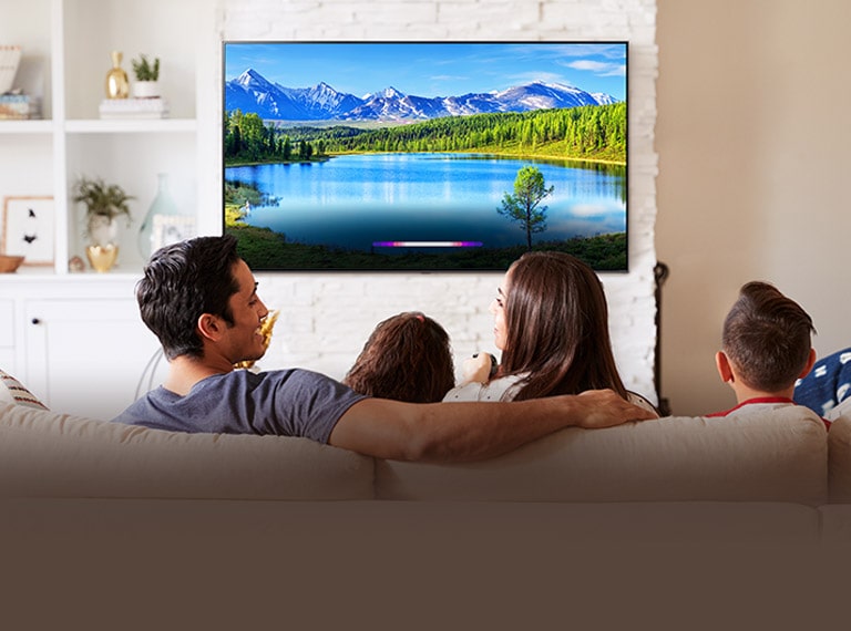 Family in bright living room looking at landscape on wall-mounted TV