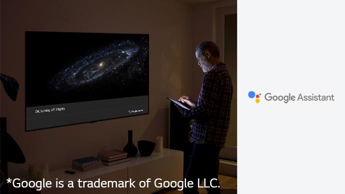 A man is standing in front of TV and ask google assistant to turn off the light