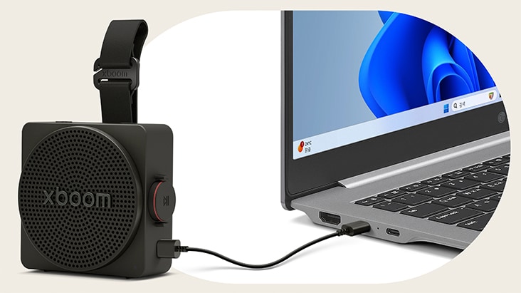 An LG gram laptop connected to the LG xboom Rock speaker via a USB-C cable, illustrating lossless audio playback through a wired connection.