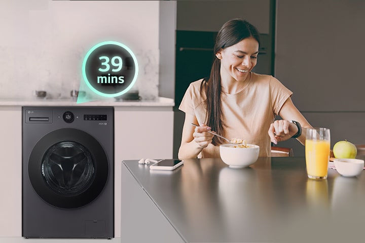 The woman is sitting at the table looking at her watch, and there is a washing machine behind her