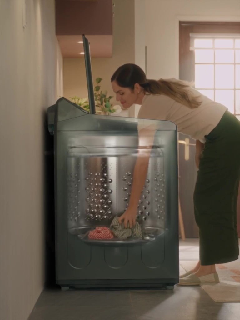 Woman unloading laundry from a top-load washer with a tilted drum structure for easier reach and access