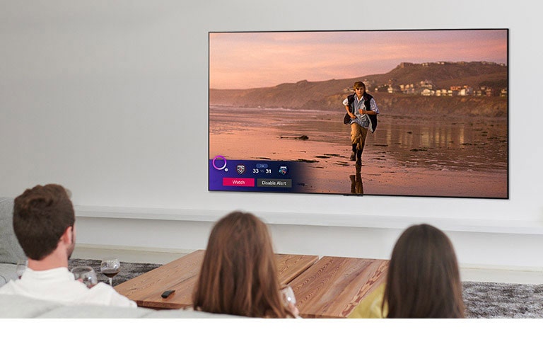 Three people watching TV screen showing a scene from a fantasy movie with a Sports Alert