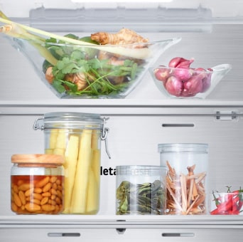 Close up view of LG bottom freezer shelf with various fresh herbs, vegetables, and preserved foods in glass containers.