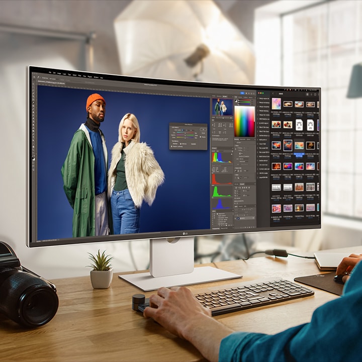 A guy is working with design program on UltraFine Monitor. A camera is placed next to the monitor.	