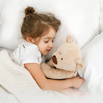  A little girl is lying in bed with a doll in her arms