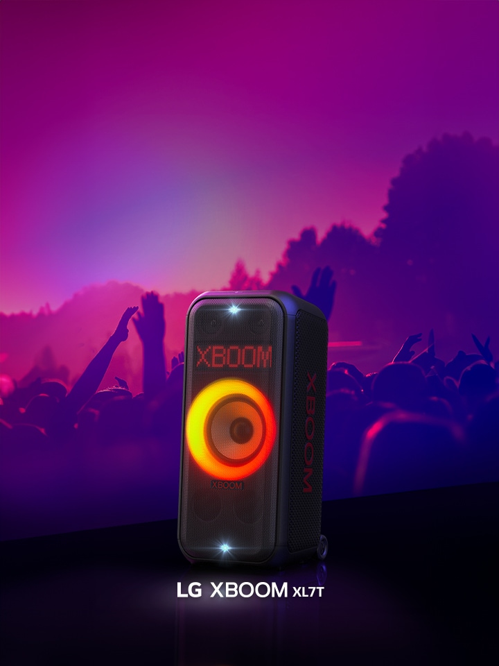 LG XBOOM XL7T is placed on the stage with red-orange gradient lighting is on. Behind the stage, people enjoy the music.