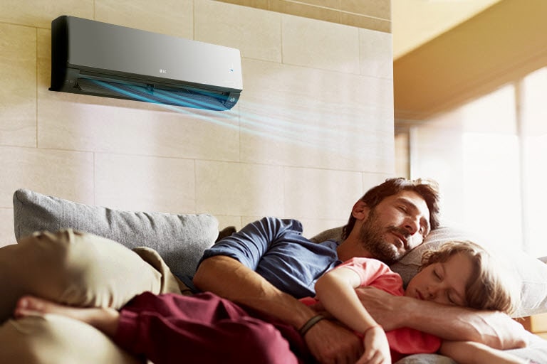 Ojciec i córka śpią na kanapie pod klimatyzatorem, który nawiewa na nich powietrze.