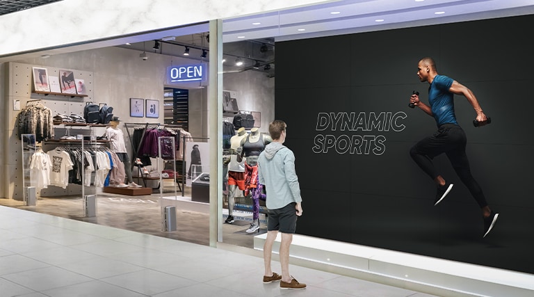 Mężczyzna patrzący na duży ekran przyczepiony do okna sklepu sportowego.