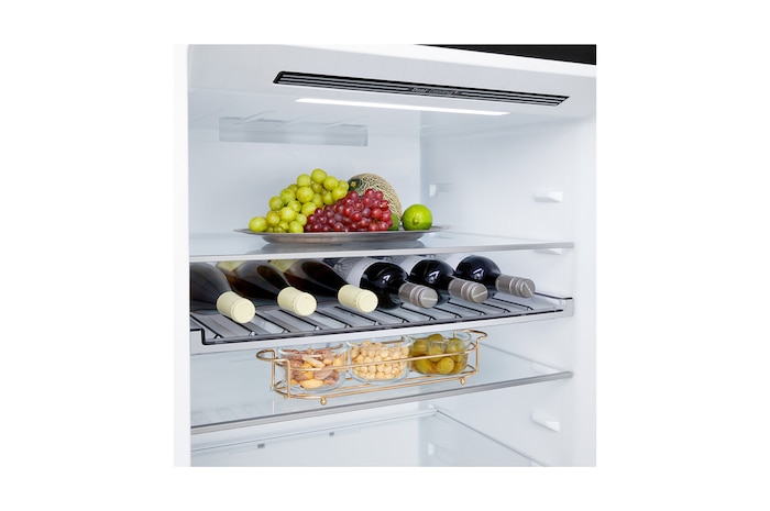 Lodówka LG z dolną zamrażarką w przestrzeni mieszkalnej z widokiem na miasto nocą; na zdjęcie nałożono grafikę przedstawiającą tryb oszczędzania energii AI oraz wykres zmiennego zużycia energii.