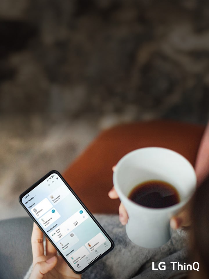 Osoba trzymająca smartfon z aplikacją LG ThinQ, pijąc kawę.