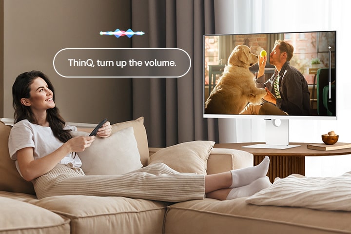 Kobieta zwiększa głośność inteligentnego monitora LG za pomocą pilota Magic.