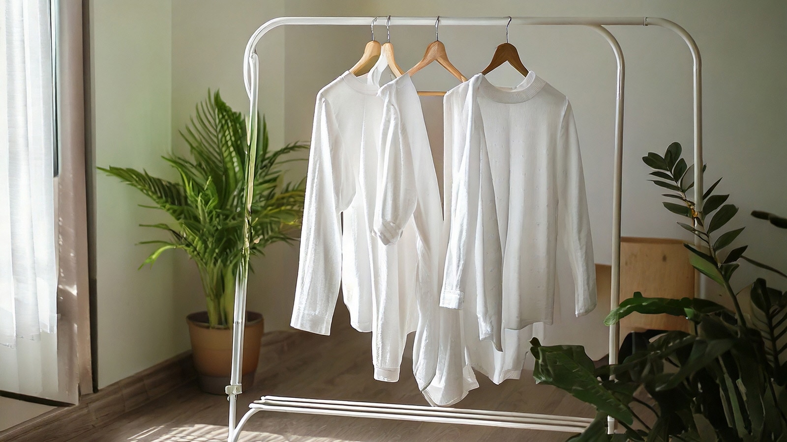 Several white long t-shirts are hanging on a drying rack in the living room.