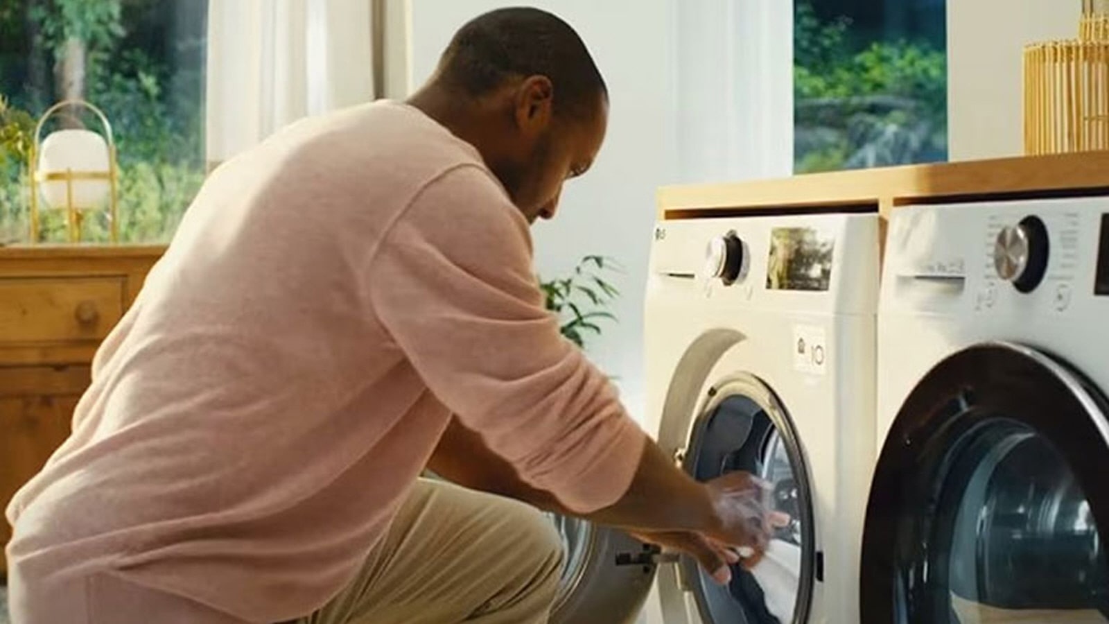 Image of a man in pink sweater trying to put hands in the white lg washing machine drum.