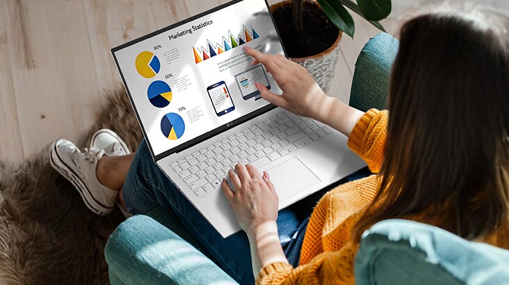A person sitting comfortably in a chair, using a laptop that displays a presentation with charts and graphs. An animation demonstrates the anti-glare screen by showing no light reflection even when sunlight shines directly onto the display.