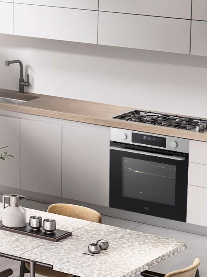 Cozinha moderna minimalista com armários brancos, forno de encastre LG e balcões em madeira, com uma mesa de refeição com centro de mesa e cadeiras.