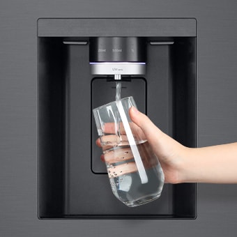 Pessoa a segurar num copo com água perto do dispensador de água do frigorífico americano com 4 portas LG.