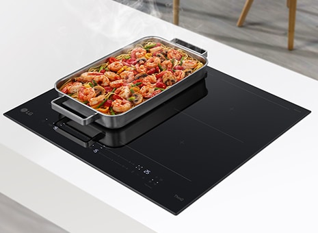 Uma ventoínha grande está localizada em dois queimadores da placa de indução. Os alimentos na panela estão a fumegar.