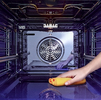 Imagem de uma pessoa a limpar o interior do forno com um pano.