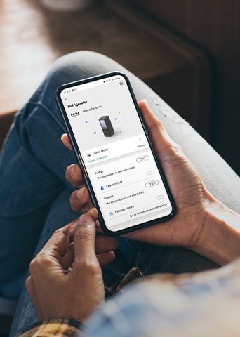 Imagem a mostrar uma app que permite manipular o frigorífico no telemóvel a ser segurado na mão.