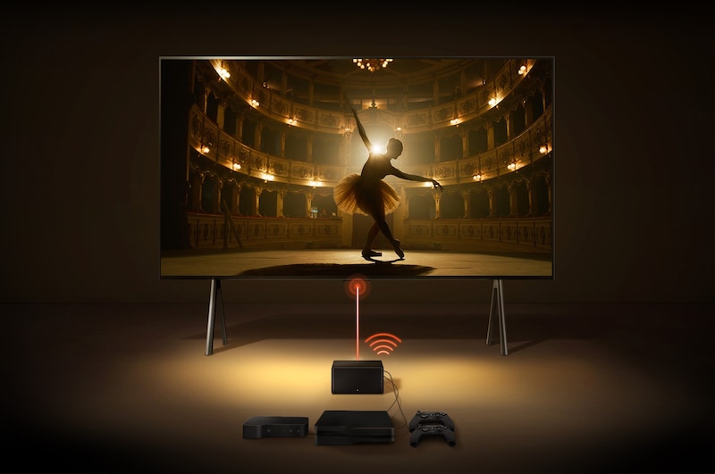 Uma Zero Connect Box em frente a um LG SIGNATURE OLED M4, com um sinal Wi-Fi vermelho e um feixe vermelho a emitir em direção à TV. A TV mostra uma bailarina a dançar a solo no palco.