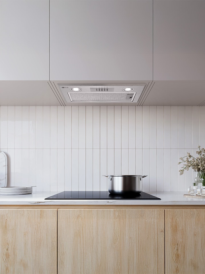 Exaustor de encastre instalado sob um armário branco por cima de uma placa numa cozinha simples.