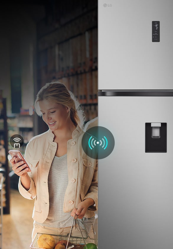 Uma mulher utiliza o seu smartphone para controlar remotamente um frigorífico LG, mostrando a sua conetividade inteligente para gerir as definições.