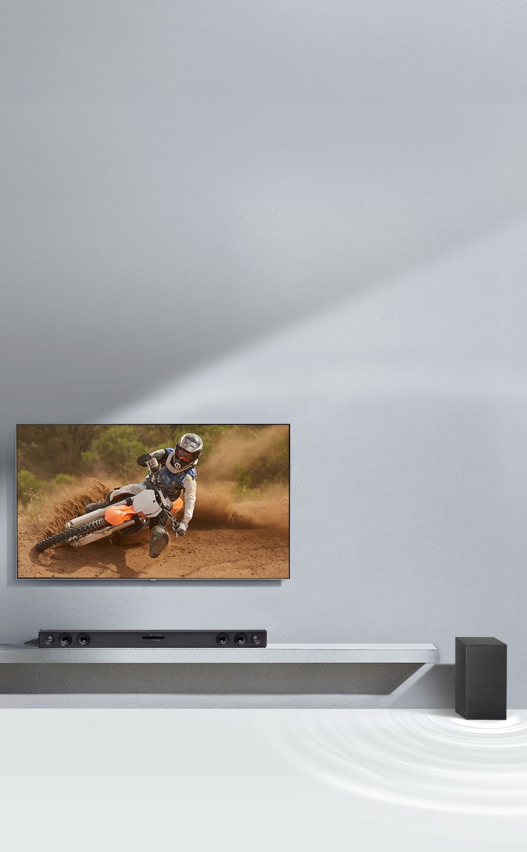 A barra de som LG SQC2 e TV LG colocadas em conjunto na sala de estar. O subwoofer está colocado ao lado da barra de som. A TV está ligada, com a imagem de uma mota.