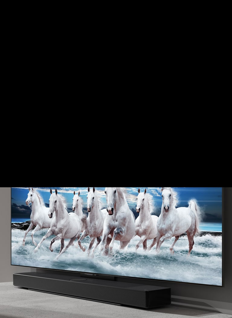 A barra de som e a TV estão colocadas sobre uma mesa branca e 7 cavalos brancos são apresentados na TV.