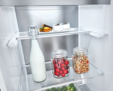 Alimentos em frascos encontram-se no interior do frigorífico e um deles é demasiado alto. Uma linha azul e setas indicam a possibilidade de dobrar a prateleira para ter mais espaço.