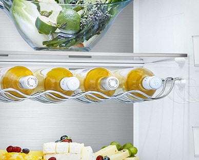 Cinco garrafas estão no suporte, por baixo da gaveta, dentro do frigorífico com outros produtos nas restantes prateleiras.