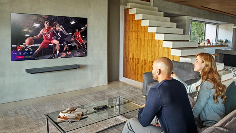 Um alerta desportivo do resultado de outros jogos aparece na parte inferior esquerda da TV enquanto um casal está a ver um jogo de basquetebol na TV