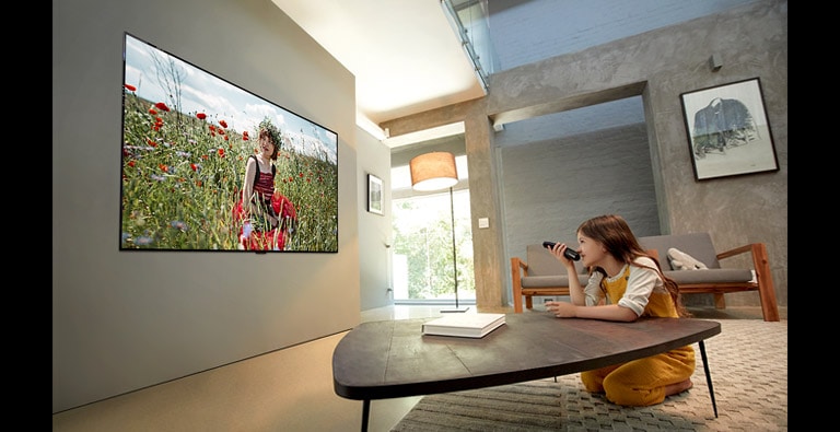 Uma menina está a ver desenhos animados em alta qualidade na TV com o braço apoiado sobre a mesa da sala de estar (mova o diapositivo)