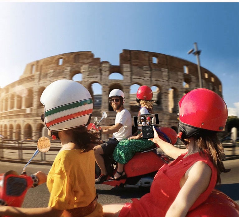 Mulher a filmar um casal numa mota do outro lado com o telemóvel.