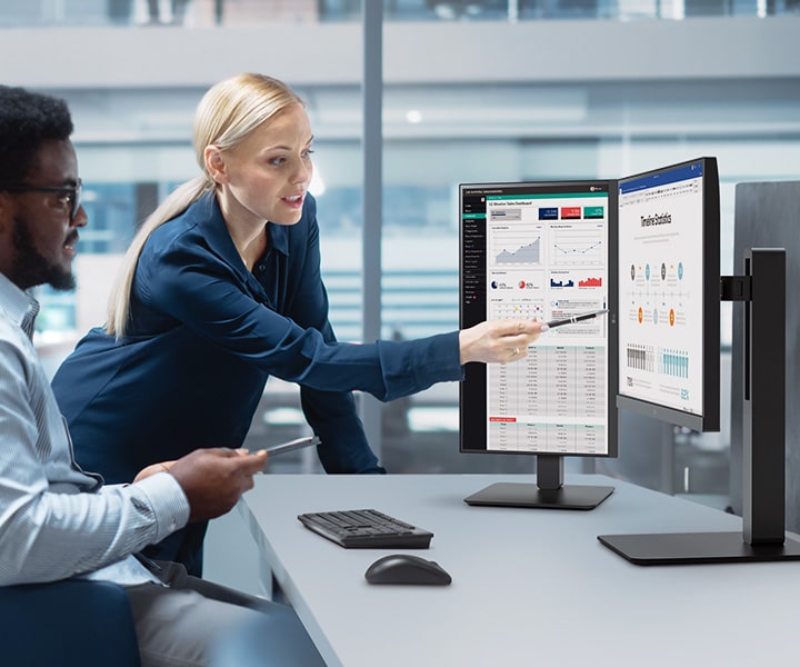 Dois funcionários, um homem e uma mulher, conversam enquanto olham para o monitor no escritório.