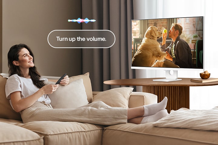 Uma mulher está a aumentar o volume do LG Smart Monitor utilizando um Magic Remote.	