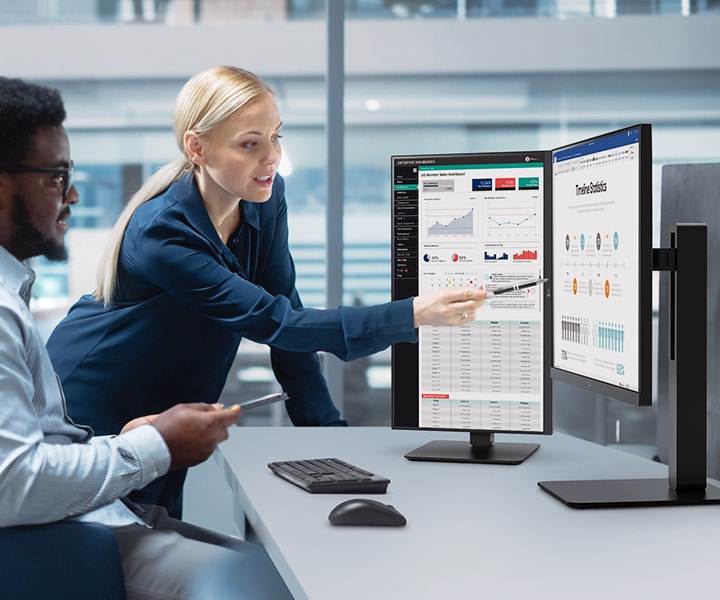 Dois funcionários, um homem e uma mulher, conversam enquanto olham para o monitor no escritório.