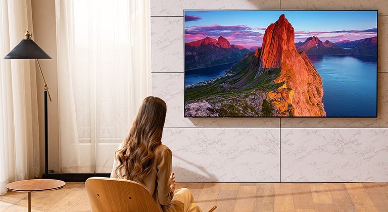 Uma mulher vê televisão na sala de estar. Paisagem no ecrã.