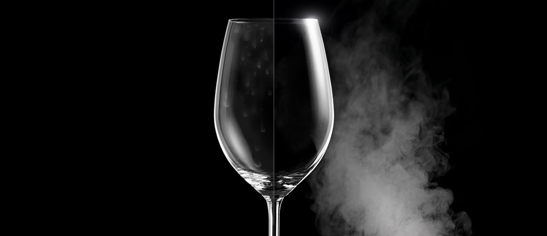 Um copo de vinho com manchas de água de um lado, e limpo e cristalino do outro após a lavagem a vapor.
