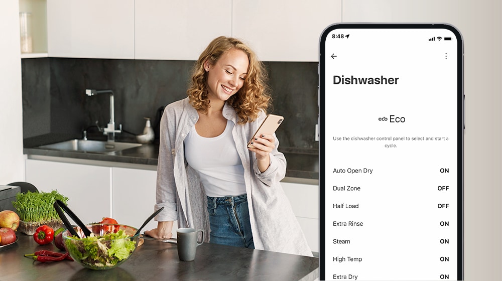 Uma mulher olha para o seu telemóvel na cozinha e o smartphone mostra as definições de personalização na aplicação ThinQ™.