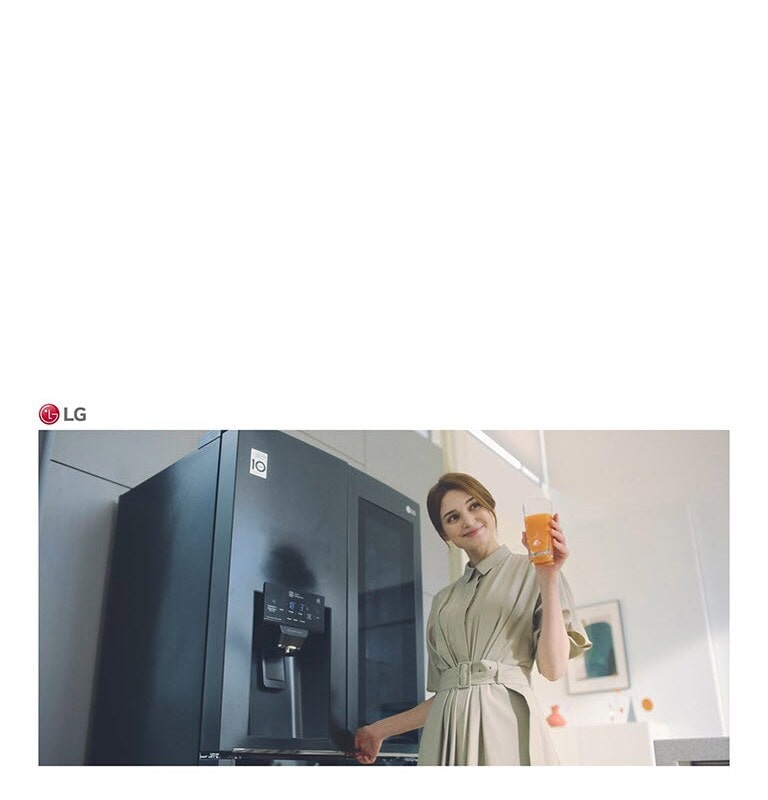 Uma mulher em frente ao frigorífico com um copo de sumo na mão e a sorrir enquanto fecha a porta.