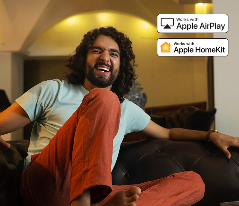 Um homem está muito divertido a assistir a algo. Logótipo do Apple AirPlay e do Apple HomeKit no canto superior direito. 