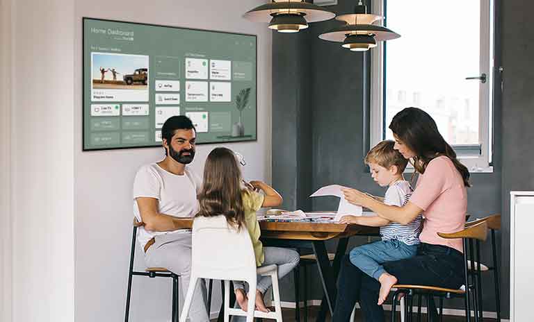 Família sentada à mesa com a mãe a perguntar à televisão o tempo que falta para o forno terminar.