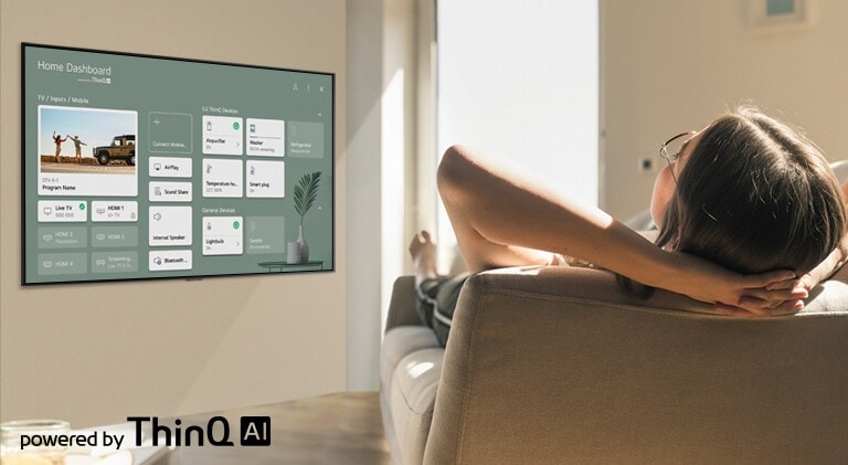 Mulher deitada no sofá a dizer à televisão para baixar a temperatura com o Home Dashboard no ecrã de televisão.