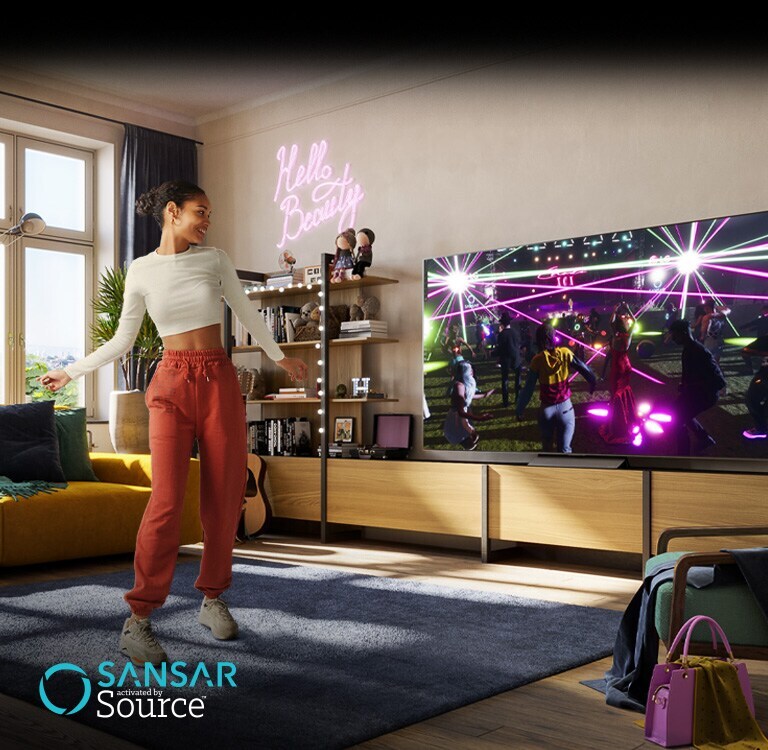 Uma mulher está a dançar na sua sala a ver um concerto no ecrã no metaverse de "Sansar" na TV