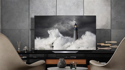 A LG OLED B2 está numa sala cinza com paredes de pedra, acessórios e cadeiras viradas para si