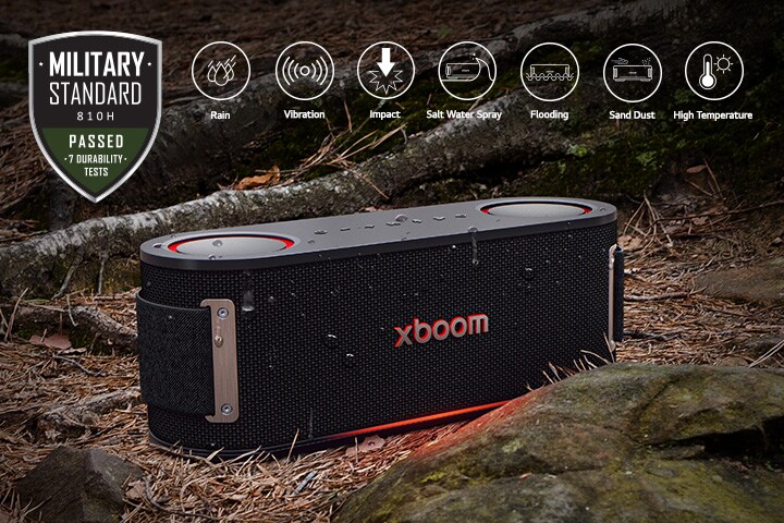 يستقر XBOOM Bounce فوق تربة تغطيها أوراق مبللة، بين جذع شجرة وحجر. يظهر شعار المعيار العسكري في الزاوية اليسرى. 